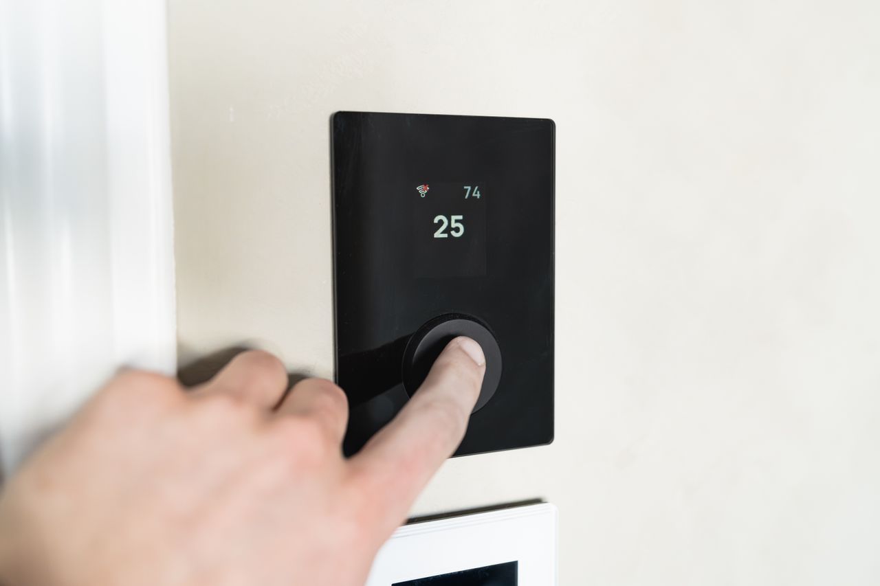 The Art of Drawing Readers In: Your attractive post title goes here Close-up of a hand adjusting a sleek, modern smart thermostat on a wall.